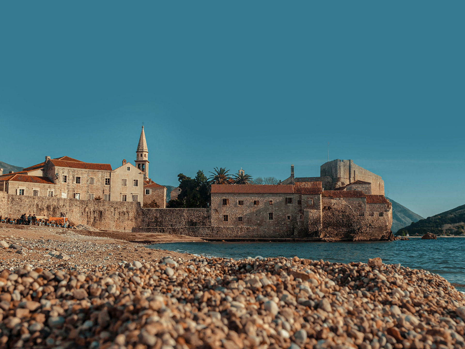 Budva old town stone walls and bell tower seen from the pebble beach