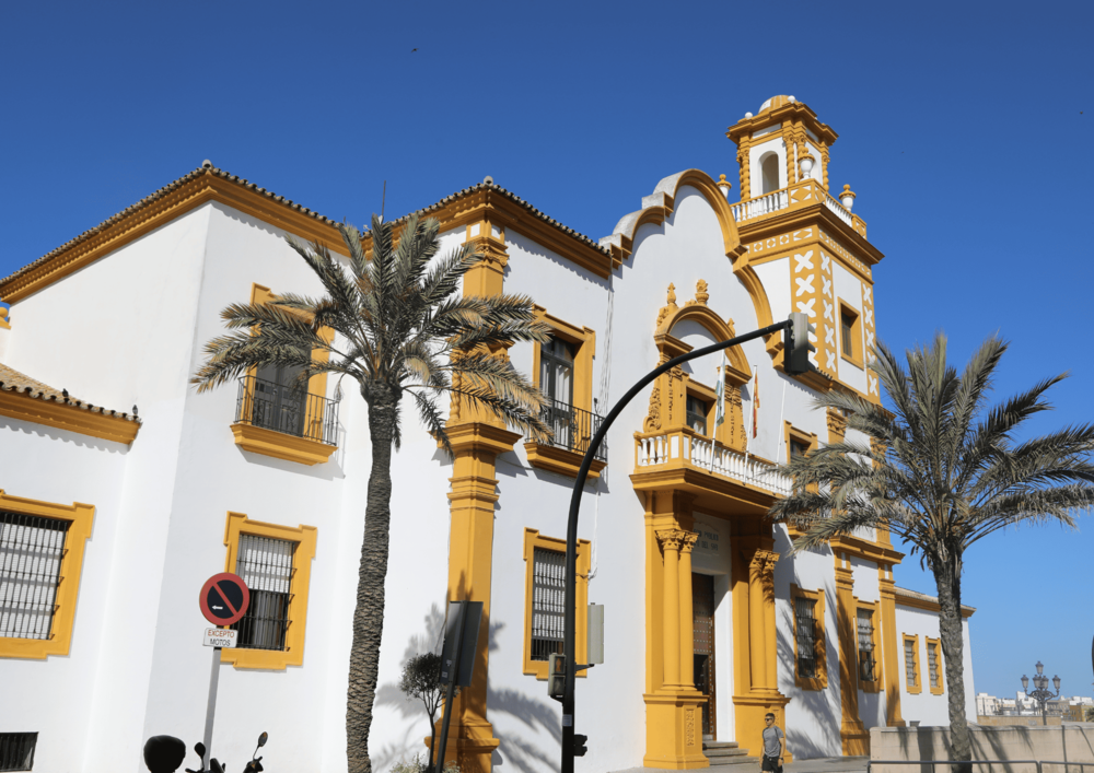 Historic yellow and white Andalusian building with palm trees in Cadiz