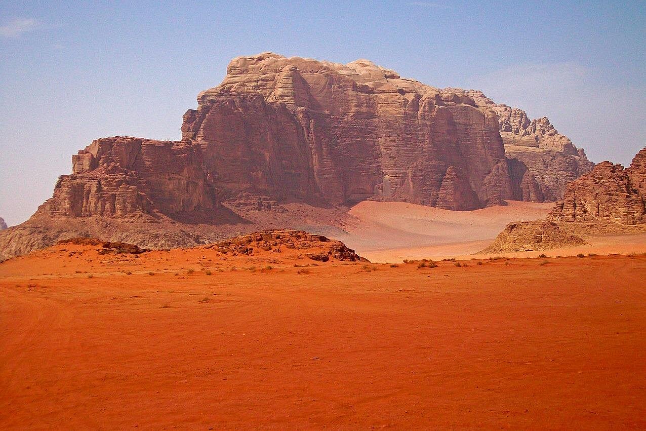 Red desert plain and monumental sandstone mountain in Wadi Rum