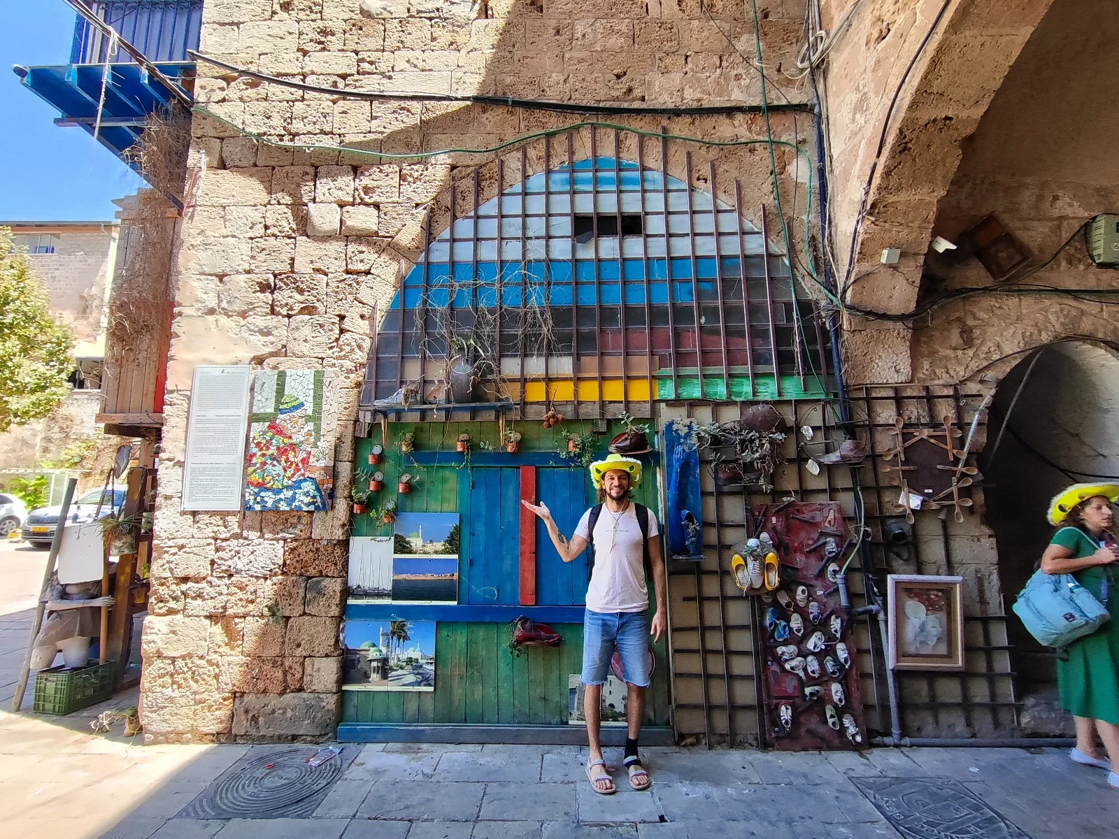Local art installation set within an ancient stone archway in an Acre alleyway, featuring painted doors and landmark photographs