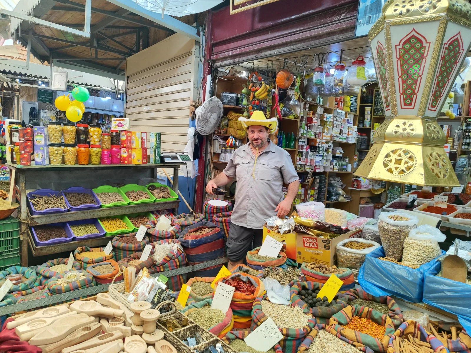Merchant in a yellow hat at a colorful spice stall in Acre's Old City market