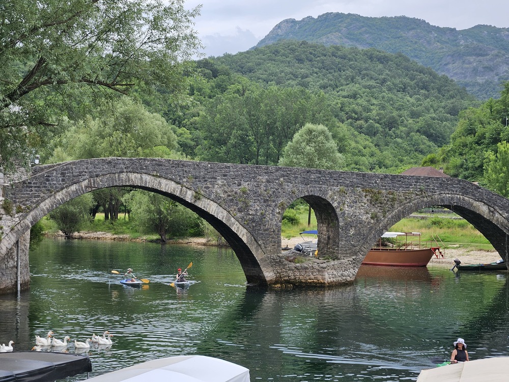 Historic stone arch bridge over the Crnojevic River with kayakers and swans