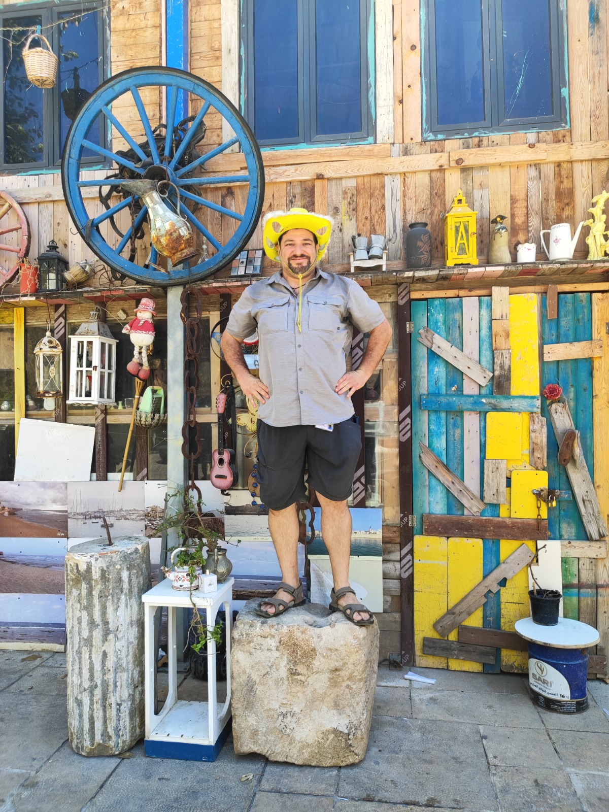 Guide in a yellow hat in front of a rustic building facade with a blue wagon wheel in Haifa