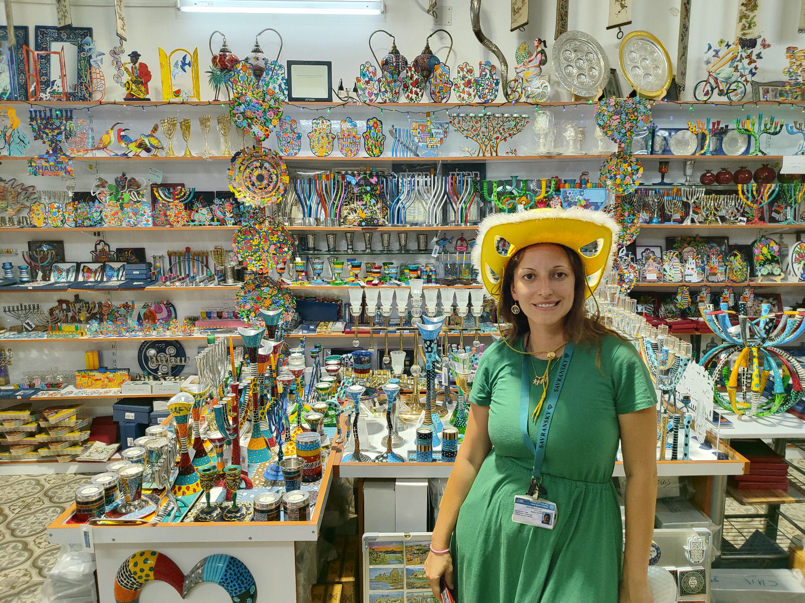 Smiling visitor in a yellow hat browsing colorful ceramic Judaica and souvenirs in an Acre shop