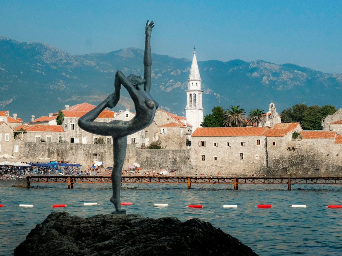 Ballerina statue on the rocks with Budva Old Town and mountains behind