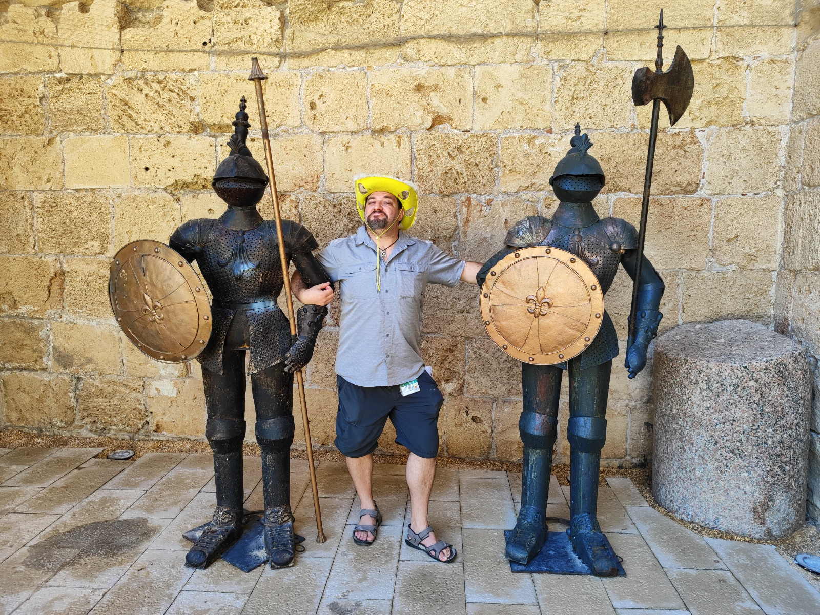Guide in a yellow hat posing between two knight statues in the Crusader city of Acre