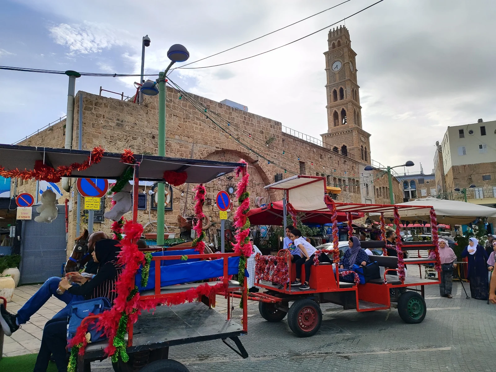 Festive red carriages carrying passengers through Old Acre with the Ottoman Khan al-Umdan clock tower in the background