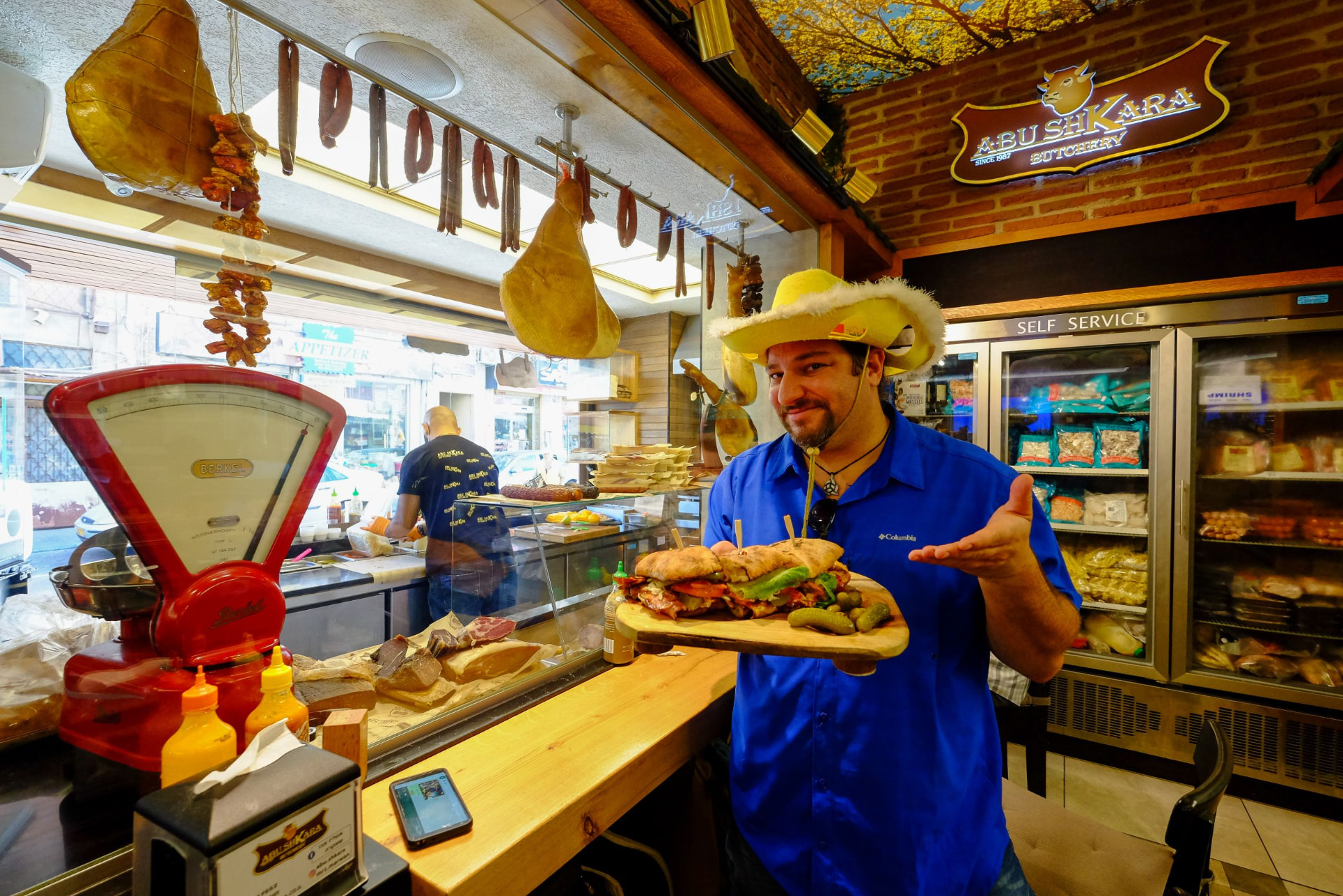 Guide in a yellow hat holding a sandwich at Abu Shkara Butchery in Haifa